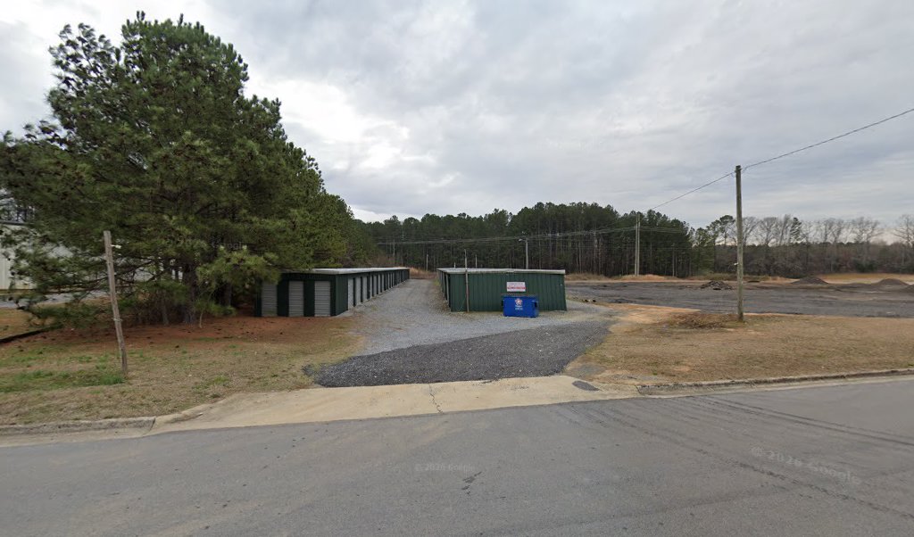 Gravel drive between two rows of green metal storage buildings with gray roll-up doors at Johnson Self Storage in Rome, GA